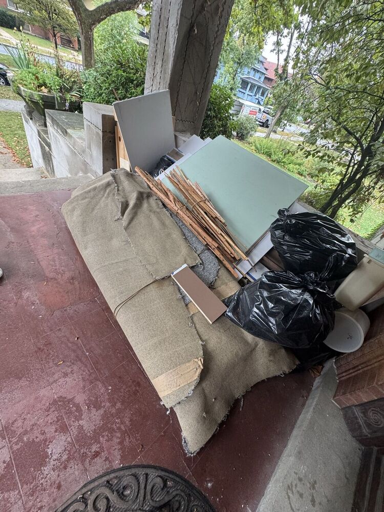 Front porch piled with old carpet, lumber, and bagged junk before 708 JUNK pickup